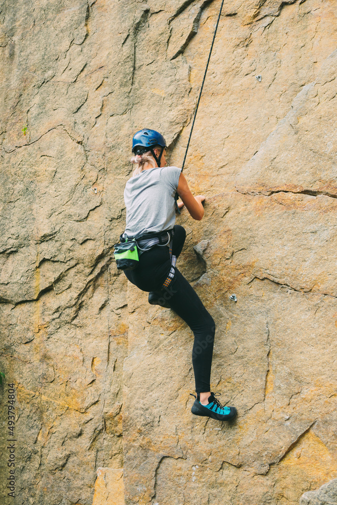 Young athletic woman in equipment doing rock climbing outdoors. Training area for outdoor activities. Extreme sport.