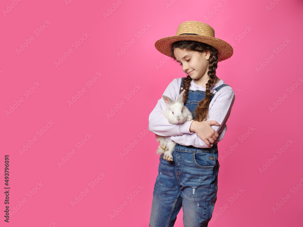 Adorable little girl in straw hat, holding a real cute bunny, looking at camera, isolated pink background. Adorable little girl in straw hat, holding a real cute bunny, looking at camera, isolated pink background.