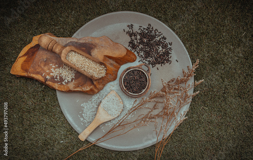 Various types of rice : Brown rice, Jasmine rice, Riceberry and dried flowers put on ceramic plate over green grass. Organic raw rice collection, Healthy food and diet concept, Overhead view, Selectiv photo