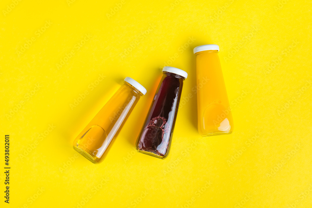 Bottles with yellow and red liquid halthy beverage on yellow background. Orange apple cherry juice Bottles with yellow and red liquid halthy beverage on yellow background. Orange apple cherry juice