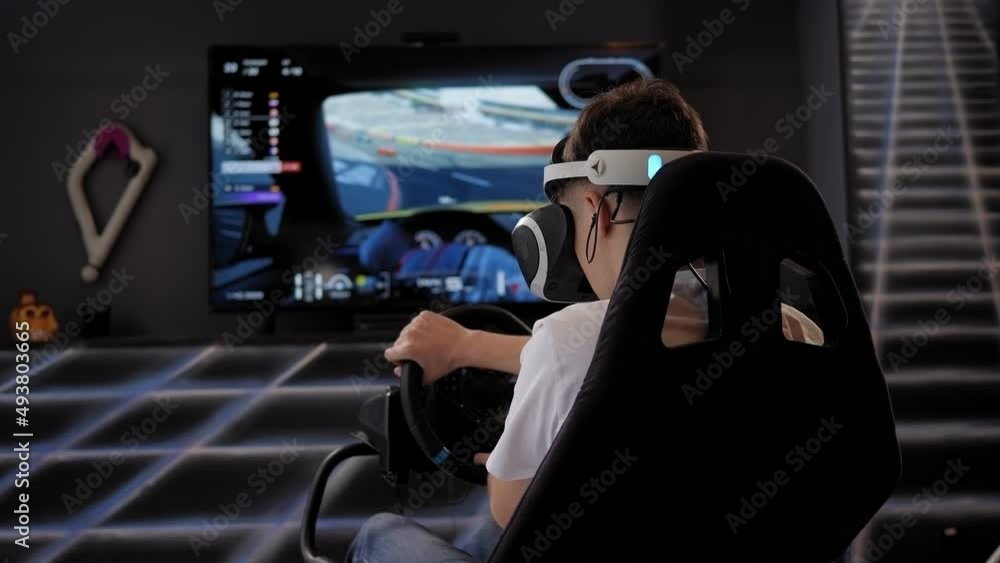A teenager in virtual reality glasses turns the steering wheel while playing a video game, a car driving simulator. A teenager in virtual reality glasses turns the steering wheel while playing a video game, a car driving simulator.
