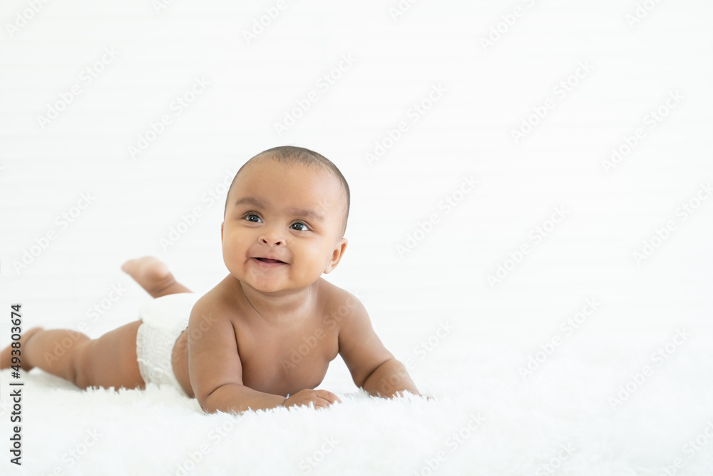 Adorable newborn Nigerian Asian baby girl wear diaper smiling with sparkling bright eyes and crawling on fluffy carpet on bed at home. White background. Copy space Adorable newborn Nigerian Asian baby girl wear diaper smiling with sparkling bright eyes and crawling on fluffy carpet on bed at home. White background. Copy space