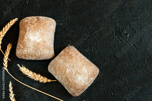 Italian ciabatta bread in the form of small two square buns on a black concrete background with copy space. Selective focus, natural light