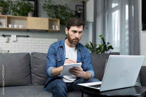 Male freelancer teaches remotely, uses laptop, looks at webcam, explains economic theory to students