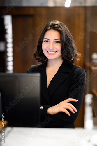 Happy female receptionist standing at hotel counter photo