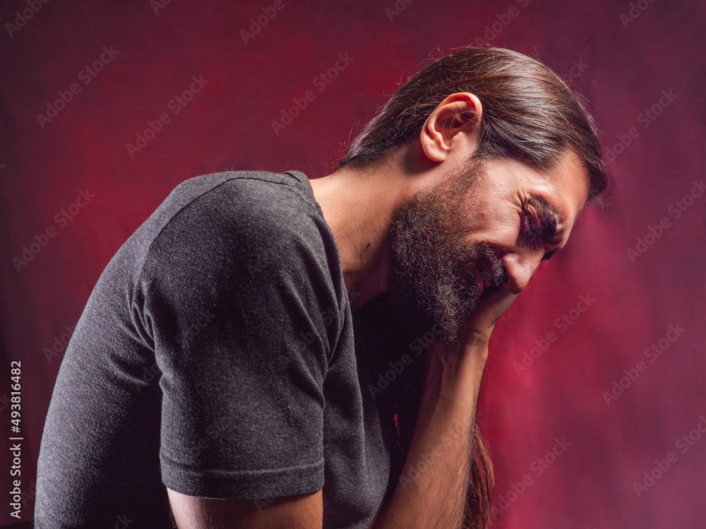 long-haired, bearded man with headache on red background