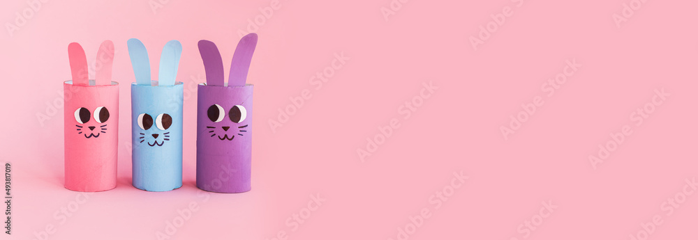 Holiday easy DIY craft idea for kids. Toilet paper roll tube toy's cute rabbit's on pink background banner. Creative Easter, Christmas decoration eco-friendly, reuse, recycle handmade minimal concept