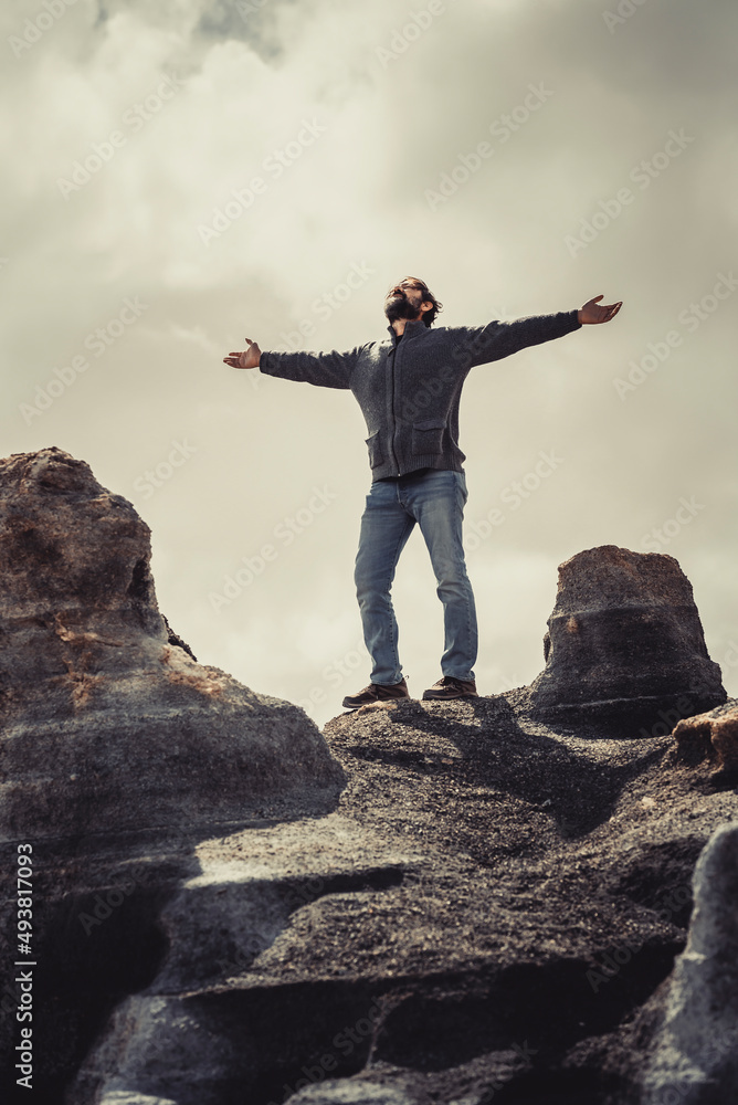 Obraz premium Man standing with arms outstretched against a cloudy grey background on old scenic stones. Concept of freedom and travel destination holiday. People enjoying life. Happiness and success life image