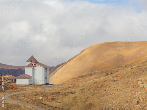 A white house with narrow windows stands high in the mountains against the backdrop of thick white clouds on a november afternoon. Journey to the countryside of the Caucasus