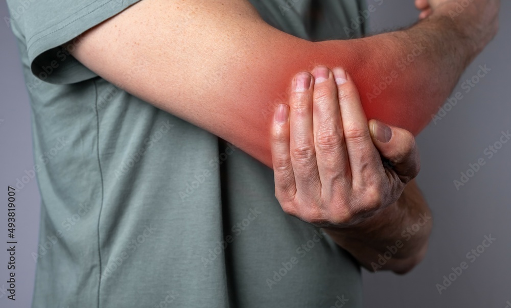 Fototapeta premium Man suffering from elbow pain and holding painful hand with red point closeup. Hand injury. Health care, joint diseases concept. High quality photo
