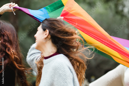 LGBT pride: lesbian couple laughing on parade. Focus on rainbow flag.
