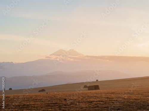 Elbrus in the distance against the twilight sky among clouds, mountain ranges and golden fields