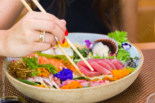 Woman eating delicious sashimi, closeup on chopsticks.