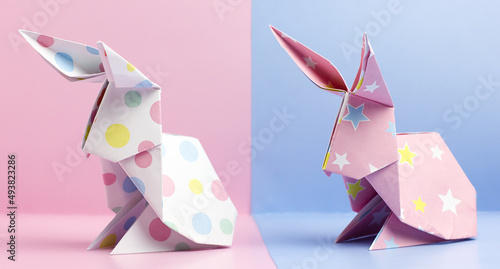 Two origami Easter bunnies on a pink and blue background