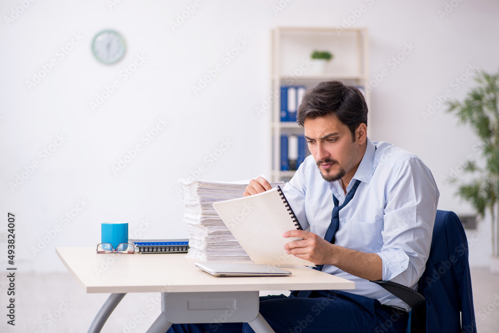 Young male employee and too much work in the office Young male employee and too much work in the office