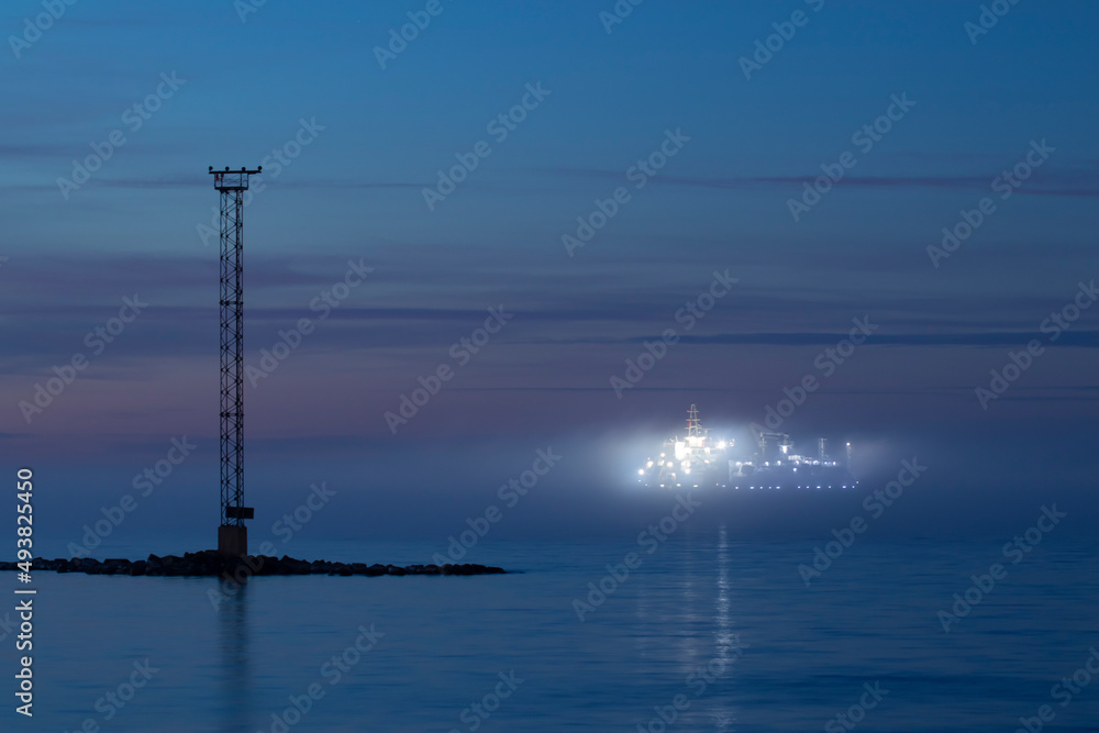 A big illuminated ship navigating in thick fog  near an island in the night after sunset with copy space