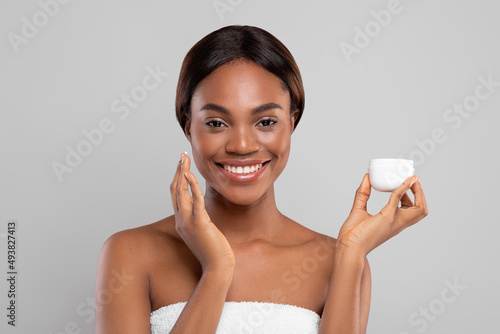 Beautiful Black Female Holding Jar With Moisturizing Cream And Applying On Face