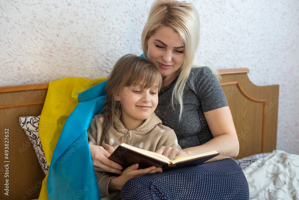 mother and daughter reading a book with the flag of ukraine in bed mother and daughter reading a book with the flag of ukraine in bed