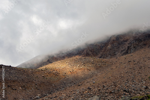 Mountains in a dense fog. Mystical landscape with beautiful sharp rocks in low clouds. Beautiful mountain foggy scenery on abyss edge with sharp stones.