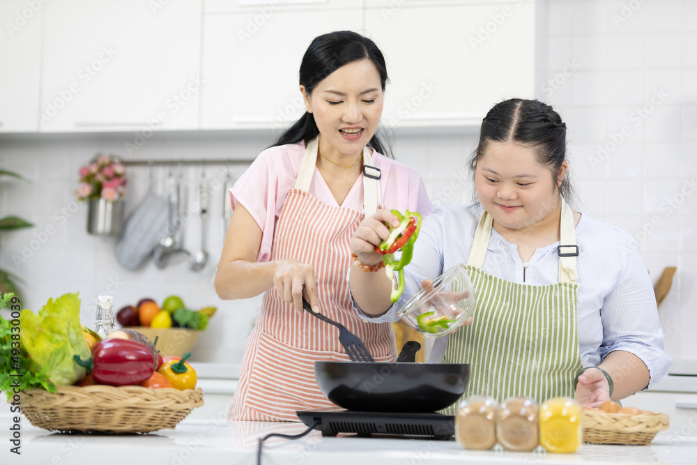 mother support down syndrome teenage girl or her daughter cooking food and frying pan on kitchen table mother support down syndrome teenage girl or her daughter cooking food and frying pan on kitchen table