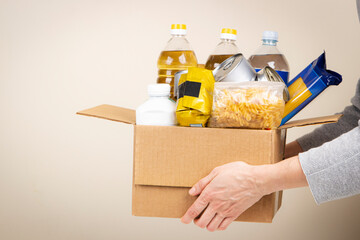 Woman hands holding cardbox with grocery products. Volunteer collecting food into donation box. Donation, charity, food bank, help for poor families, migrants, refugees