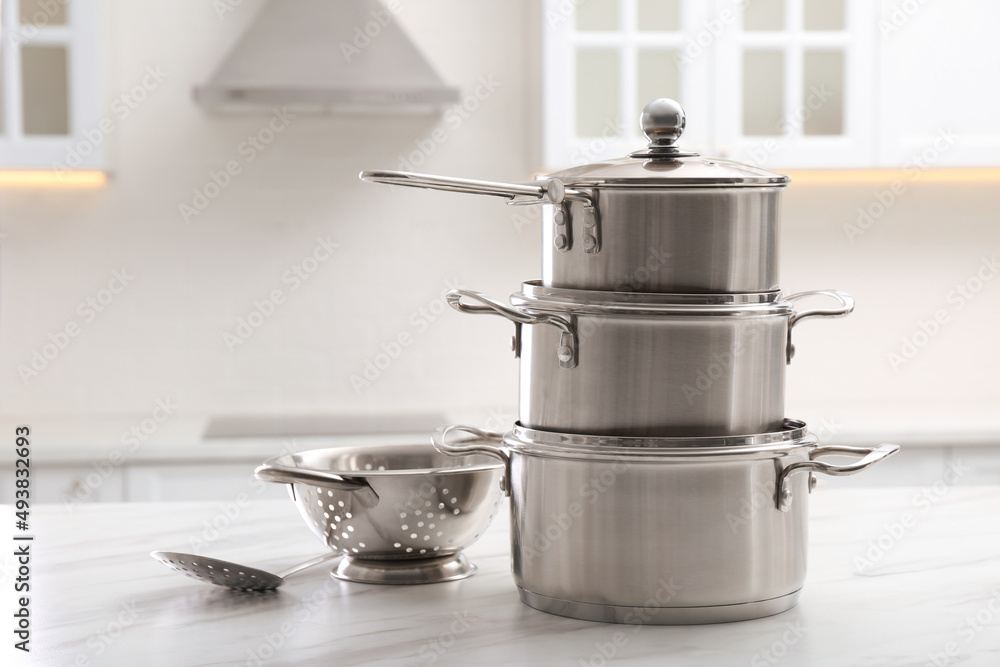 Set of stainless steel cookware and kitchen utensils on white table indoors Set of stainless steel cookware and kitchen utensils on white table indoors