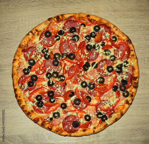 Baked, round pizza with salami, pepperoni and sliced olives with brown crust.