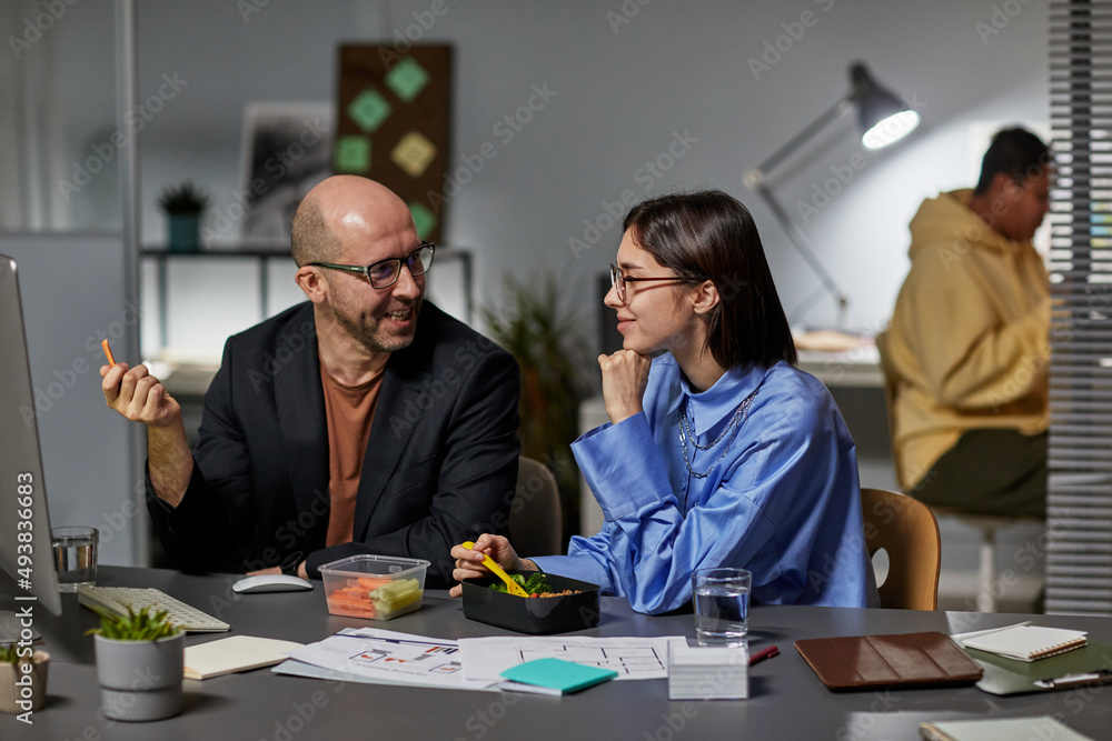Portrait of smiling adult man talking to female colleague while working together late in office