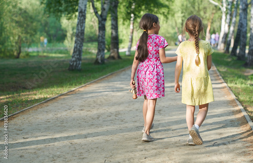 A photo from the back of two little girls sisters walking together on a path in the park. The concept of children's love and friendship, best friends forever. High quality photo