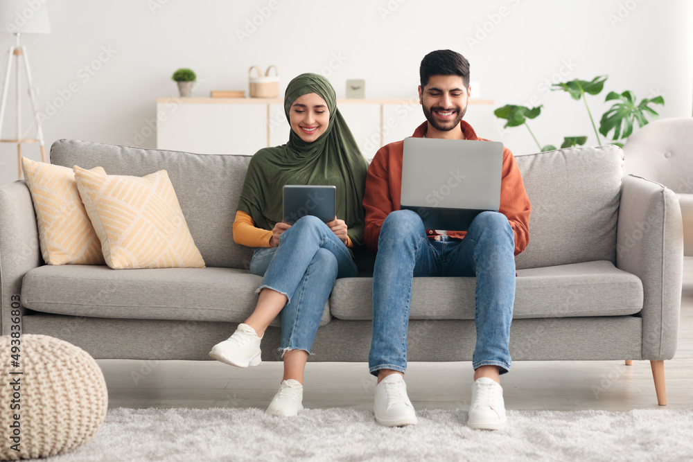 Millennial Arabic Spouses Using Laptop And Digital Tablet At Home Millennial Arabic Spouses Using Laptop And Digital Tablet At Home