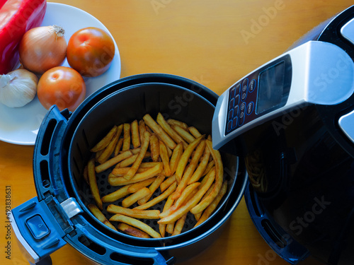 Top view of an air fryer on a table with french fries and vegetables.
