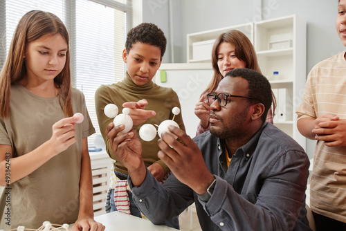 Side view portrait of African American teacher explaining molecule structure to diverse group of children in chemistry class photo