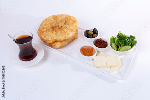 Cropped view of plate of greens, tomato paste, olives, citrus jam, cheese slices, cup of tea and bagels on white plate, shot with selective focus on isolated white background from opposite angle.