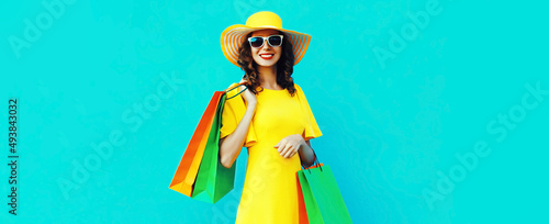 Portrait of beautiful happy smiling young woman with shopping bags wearing summer straw round hat on blue background