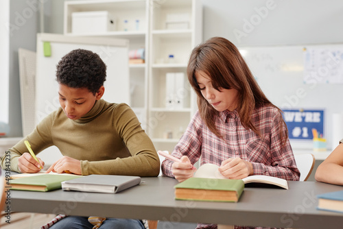 Portrait of two young girls writing in notebooks while studying in school classroom