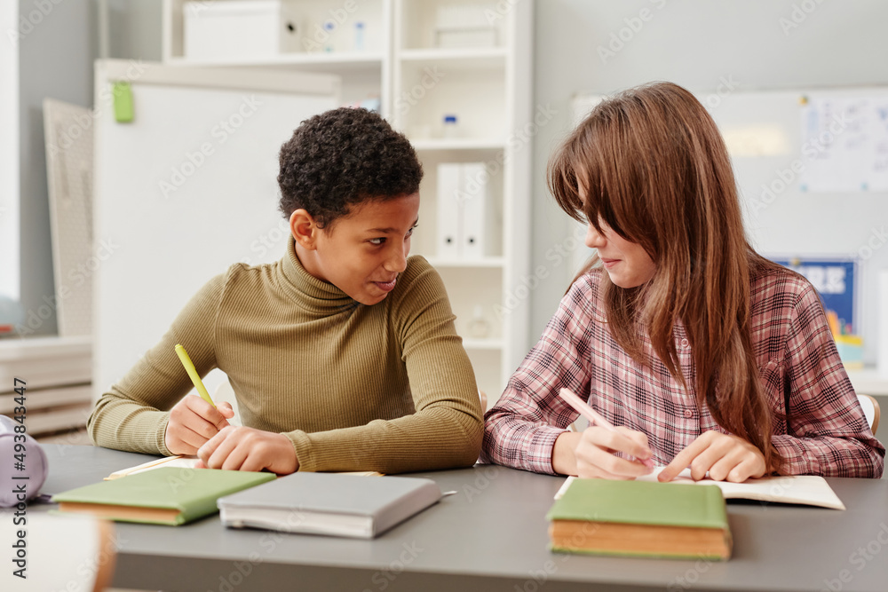 Portrait of two young girls whispering while cheating during test in school classroom Portrait of two young girls whispering while cheating during test in school classroom