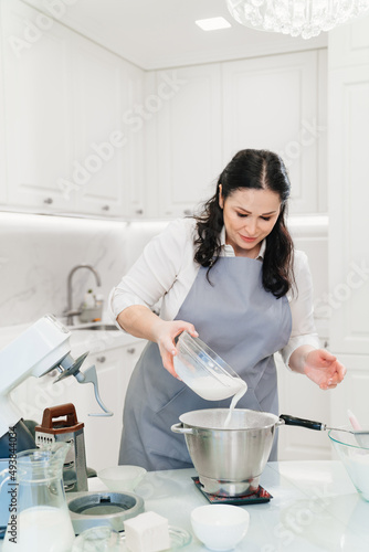 A women cook adds a milk to prepare dough or cream in a mixer bowl.