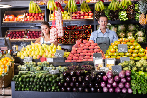 Portrait of young man and woman offering greens and vegetables in store