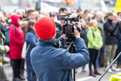 Filming street protest, television camera operator in the focus, blurred people in the background