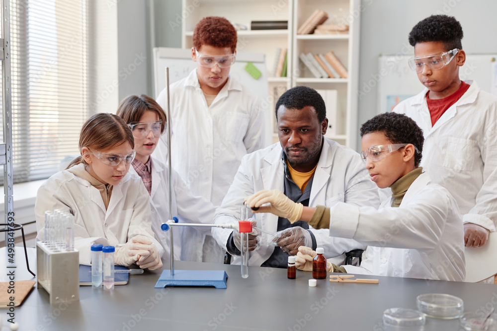 Portrait of African American teacher demonstrating science experiments to diverse group of children in chemistry lab at school Portrait of African American teacher demonstrating science experiments to diverse group of children in chemistry lab at school