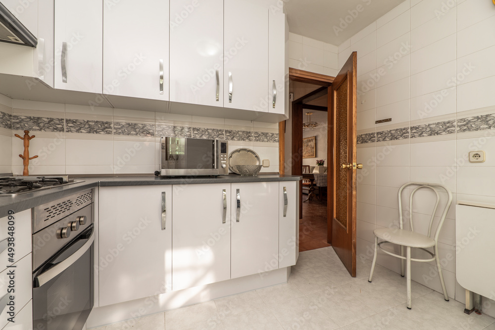 Fototapeta premium Kitchen with white furniture, gray countertop, stainless steel appliances with stoneware floors