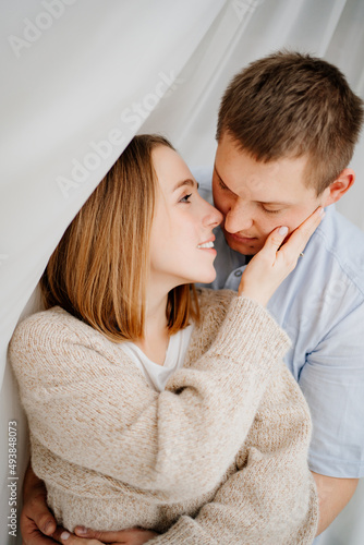 a happy and loving couple hugs against the background of a white curtain. 