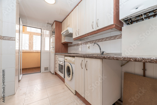 Fototapeta Naklejka Na Ścianę i Meble -  Kitchen with furniture and drawers in light tones with details in wood and pink granite countertops with white appliances and a washing machine and porcelain stoneware floors
