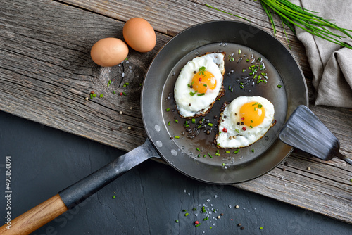 Knusprig gebratene Spiegeleier mit Schnittlauch und Salz in der Eisenpfanne rustikal serviert  – Crunchy fried egg served in an iron frying pan on rustic wood  photo