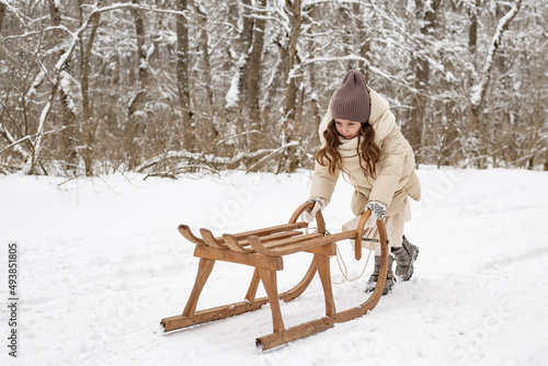 a cute six-year-old girl rolls a wooden sled on a snowy road in the park