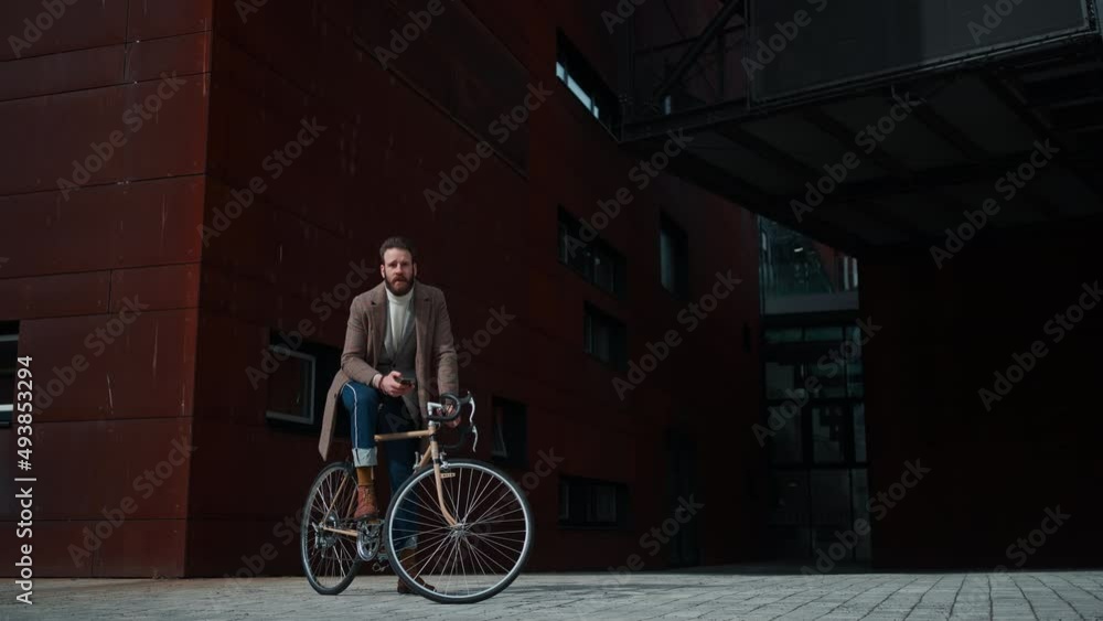 Young man with bicycle holding a smartphone front of building. copy space. Creative businessman in a modern business area. Young man with bicycle holding a smartphone front of building. copy space. Creative businessman in a modern business area.