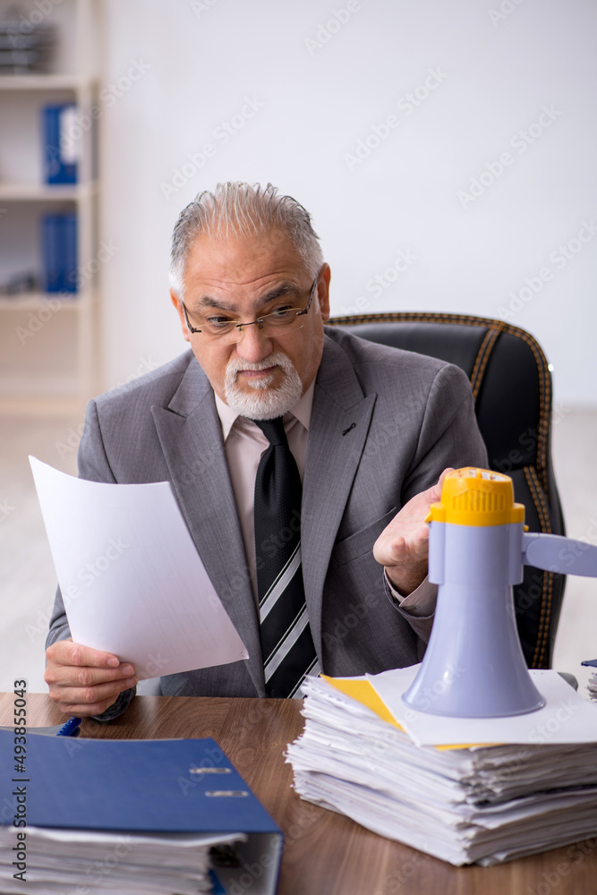 Old male employee holding megaphone in the office Old male employee holding megaphone in the office