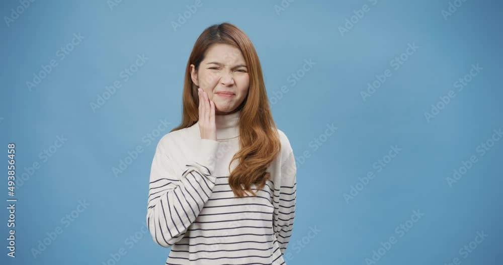 Youth Asia lady wear sweater touch mouth with hand with painful bad feel because of toothache or dental illness on teeth stand isolated over blue background. Negative emotion facial expression feel. Youth Asia lady wear sweater touch mouth with hand with painful bad feel because of toothache or dental illness on teeth stand isolated over blue background. Negative emotion facial expression feel.