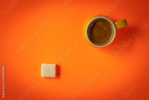 Yellow mug of freshly brewed double espresso on orange background with party size wafer on the opposite side of the frame