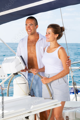 Young man and woman steering pleasure yacht, enjoying romantic sea travel on warm summer day © JackF